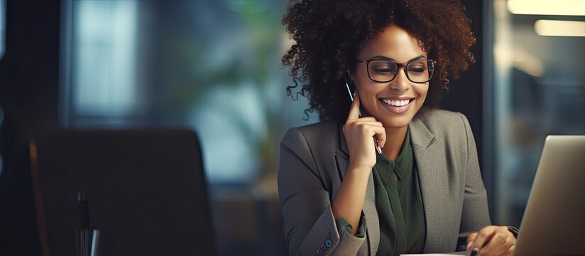 African American businesswoman smiles while working speaking on the phone and making notes in her office