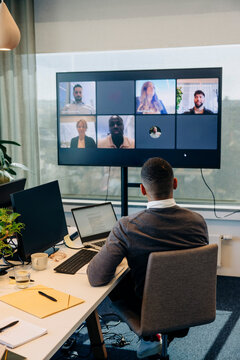 Rear view of businessman doing video conference with colleagues on TV screen in office