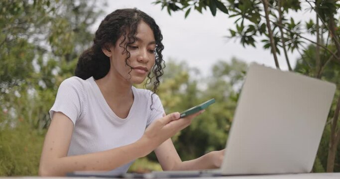 Young female freelance sitting doing online business on laptop in park. Plan an online meeting strategy via video call. Online learning with wireless internet technology
