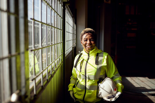 Portrait of smiling young female blue-collar worker standing by window in factory