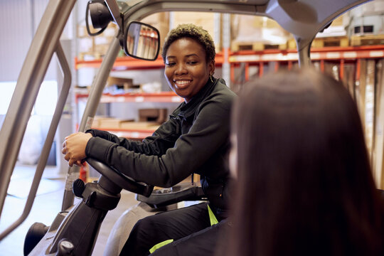 Smiling forklift operator looking at colleague in distribution warehouse