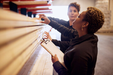 Multiracial female colleagues examining planks on rack in lumber industry