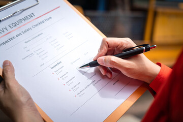 Action of a mechnical engineer is using a pen to mark at need repair on the heavy machine inspection form. Industrial service working concept. Selective focus.