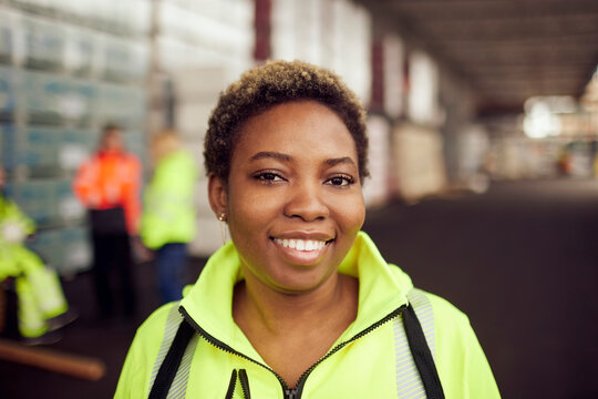 Portrait of smiling young female worker in reflective clothing at industry