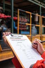 A mechanical engineer is checking on heavy machine and equipment inspection checklist form with the water pumping unit as background . Heavy industrial working action scene, selective focus.