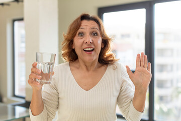 middle age pretty woman feeling happy and astonished at something unbelievable. water glass