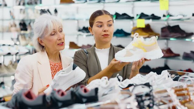 Young woman and elderly woman buying sneakers in shoe store