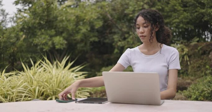 Young female freelance sitting doing online business on laptop in park. Plan an online meeting strategy via video call. Online learning with wireless internet technology