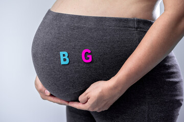 Close-up of pregnant woman touching her belly and the wooden alphabet with boy and girl on tummy...