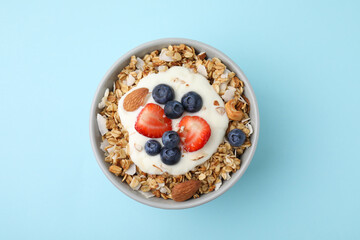 Tasty granola, yogurt and fresh berries in bowl on light blue background, top view. Healthy breakfast