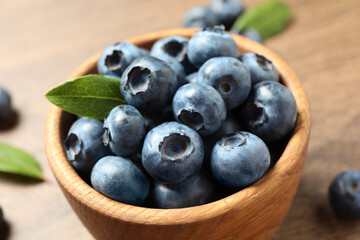 Bowl of tasty fresh blueberries with green leaves on table, closeup