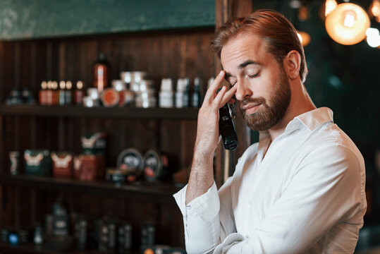 Tired, holding hair clipper. Handsome barber is in the salon