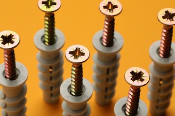 Many metal screws with dowels on orange background, closeup