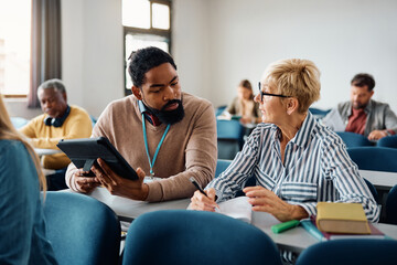 Black adult education teacher assists mature student with her assignment during class.