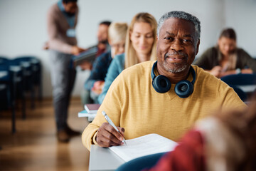 Black mature man learning on adult education training class in classroom and looking at camera.