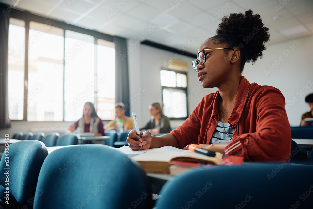 Wall mural black university student writes in her notebook during lecture in classroom.