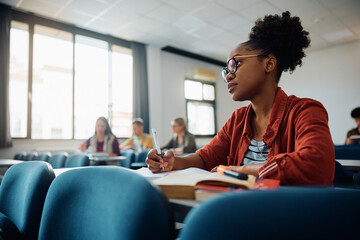 Black university student writes in her notebook during lecture in classroom.