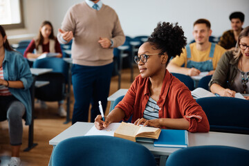 Black female student taking notes during class in lecture hall.