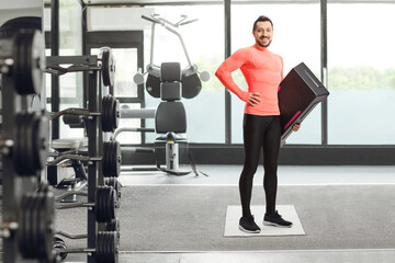 Full length portrait of a fit young man holding a step aerobic platform at a gym
