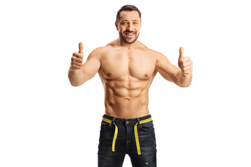 Fototapeta premium Young fit shirtless man wearing jeans with a measuring tape around waist and gesturing thumbs up