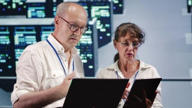 Data storage company executives looking around data center, using laptop and tablet to crosscheck contingency plan and assess high tech workspace units in need of fixing, preventing liabilities