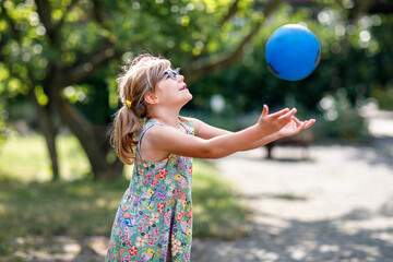 Little preschool girl with eyeglasses playing with ball outdoors. Happy smiling child catching and throwing, laughing and making sports. Active leisure with children and kids. Summer day on backyard - Powered by Adobe