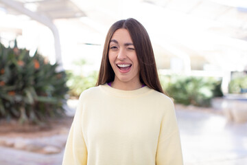 young pretty woman looking happy and friendly, smiling and winking an eye at you with a positive...