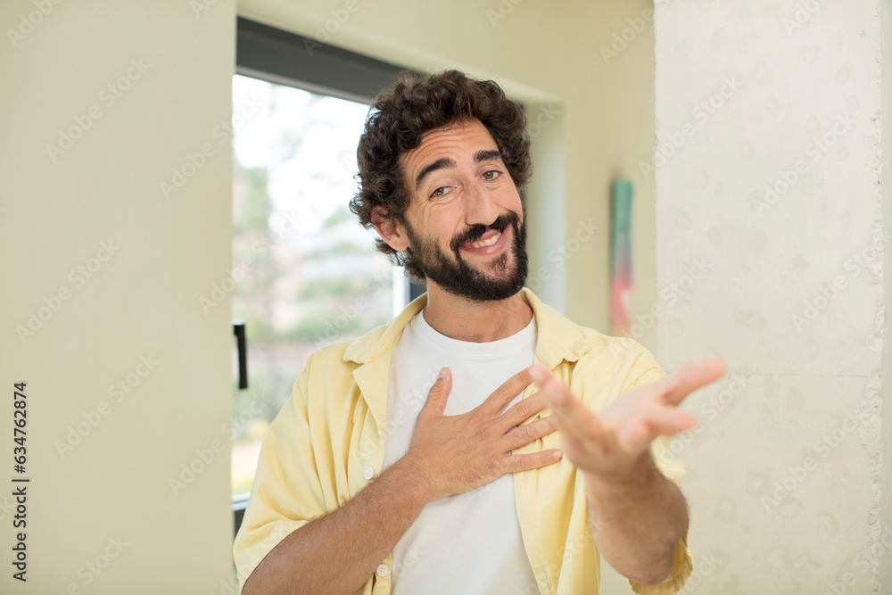 Canvas Prints young crazy bearded man feeling happy and in love, smiling with one hand next to heart and the other stretched up front