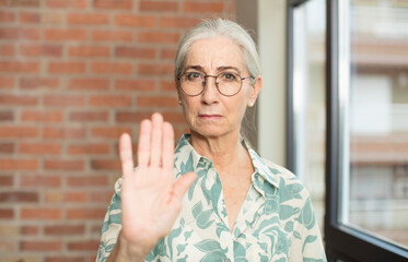 senior pretty woman looking serious, stern, displeased and angry showing open palm making stop...