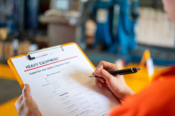 A technician worker is writing on heavy equipment inspection checklist before repairing the...