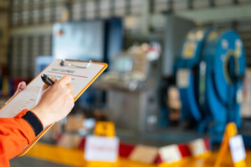A technician worker is writing on heavy equipment inspection checklist before repairing the...