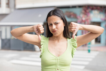 pretty hispanic woman looking sad, disappointed or angry, showing thumbs down in disagreement, feeling frustrated