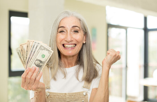 pretty senior woman feeling shocked,laughing and celebrating success. with dollar banknotes
