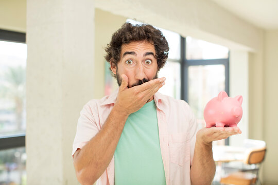 crazy bearded man covering mouth with a hand and shocked or surprised expression. piggy bank concept