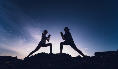Young couple does yoga exercises on edge of mountain against sunrise
