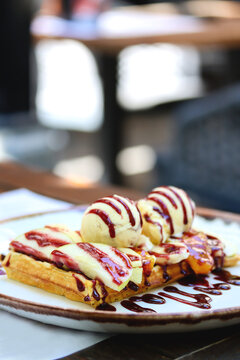 Belgian waffle with ice cream, berry sauce and fresh sliced fruits on a plate on a restaurant table. Vertical image of wholegrain flour belgian waffle with a scoop of ice cream and natural berry syrup