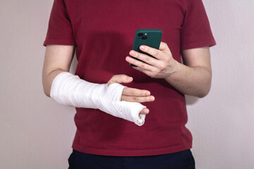 A man in a red T-shirt with a broken arm in a cast holds and uses a phone Close-up