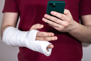 A man in a red T-shirt with a broken arm in a cast holds and uses a phone Close-up