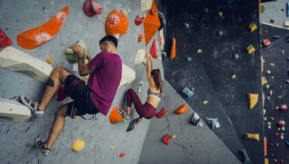 A strong couple of climbers climb an artificial wall with colorful grips and ropes.