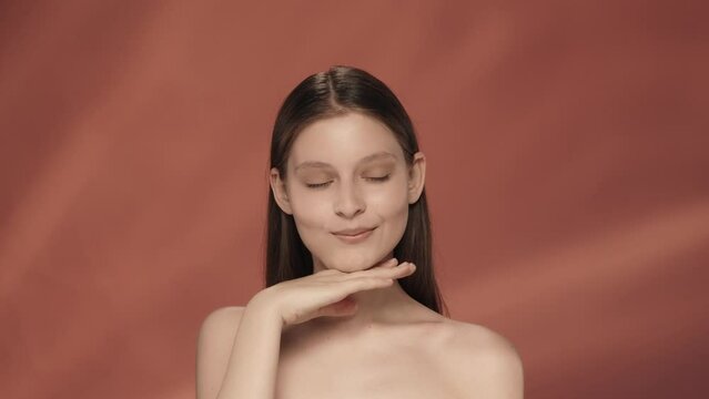 A young woman demonstrates clear skin and regular facial features. Portrait of a seminude woman in a studio on a red background close up. Facebuilding. The concept of natural beauty, cosmetology.