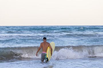 man walking into the sea with the surfboard