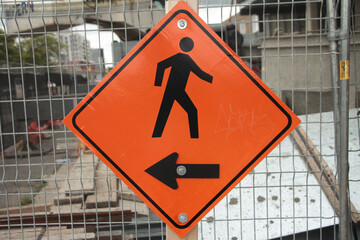 diamond orange sign with arrow pointing left and illustration of person walking right in black...