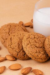 Oatmeal cookies, glass of milk and almonds on beige background.