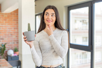 pretty young model smiling with a happy, confident expression with hand on chin. decorative cactus concept