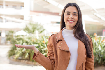 pretty young adult woman smiling, feeling confident, successful and happy, showing concept or idea on copy space on the side