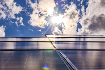 A photovoltaic system on a roof backlit with sun and clouds