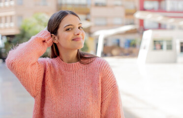 young pretty woman smiling cheerfully and casually, taking hand to head with a positive, happy and confident look