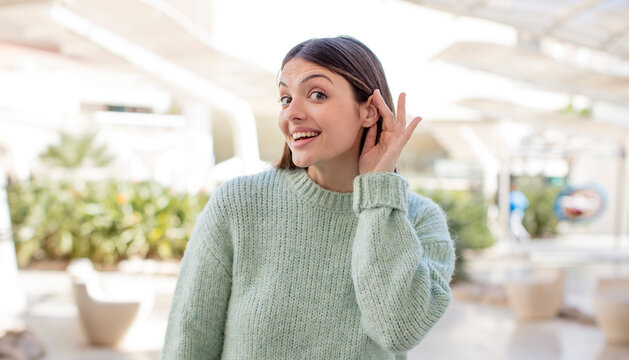 young pretty woman looking happy, listening, trying to hear a secret conversation or gossip, eavesdropping