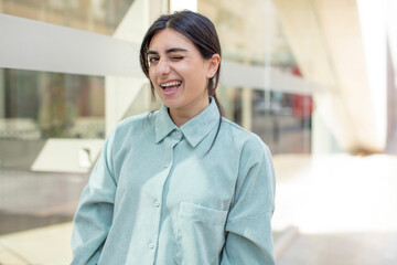 pretty woman looking happy and friendly, smiling and winking an eye at you with a positive attitude