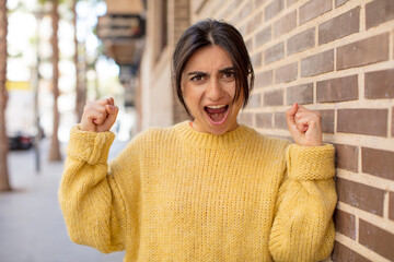 pretty woman shouting aggressively with an angry expression or with fists clenched celebrating...